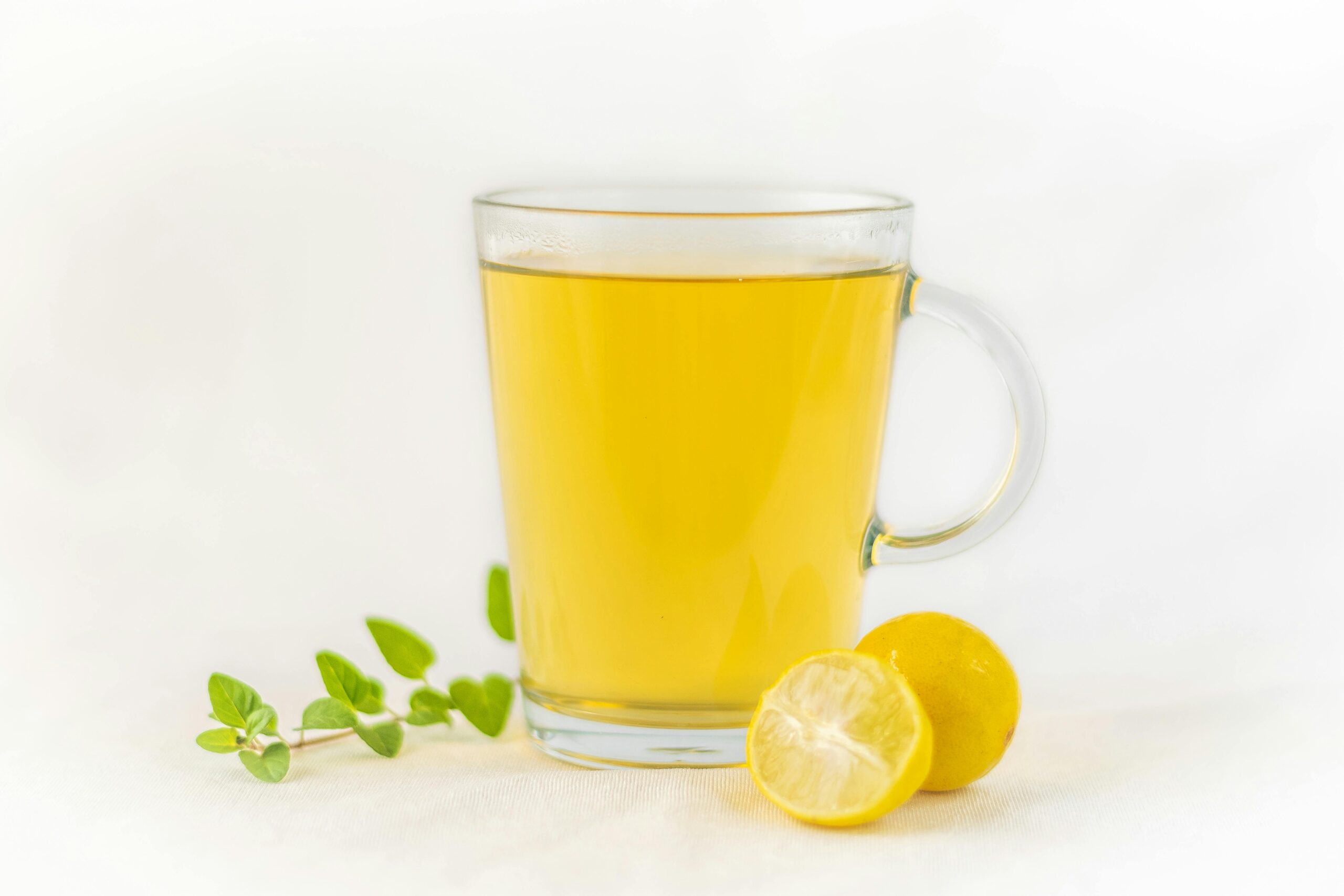 A glass of lemon tea with fresh herbs and lemon slices on a white background.