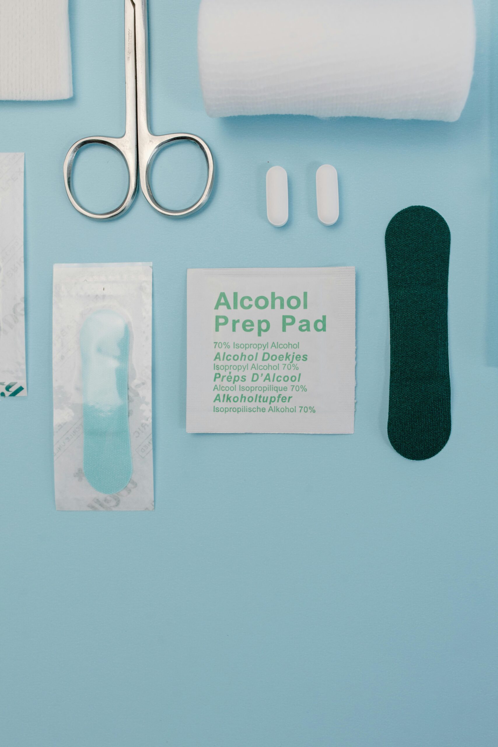 Top view of medical supplies including gauze, scissors, and alcohol prep pad on blue background.
