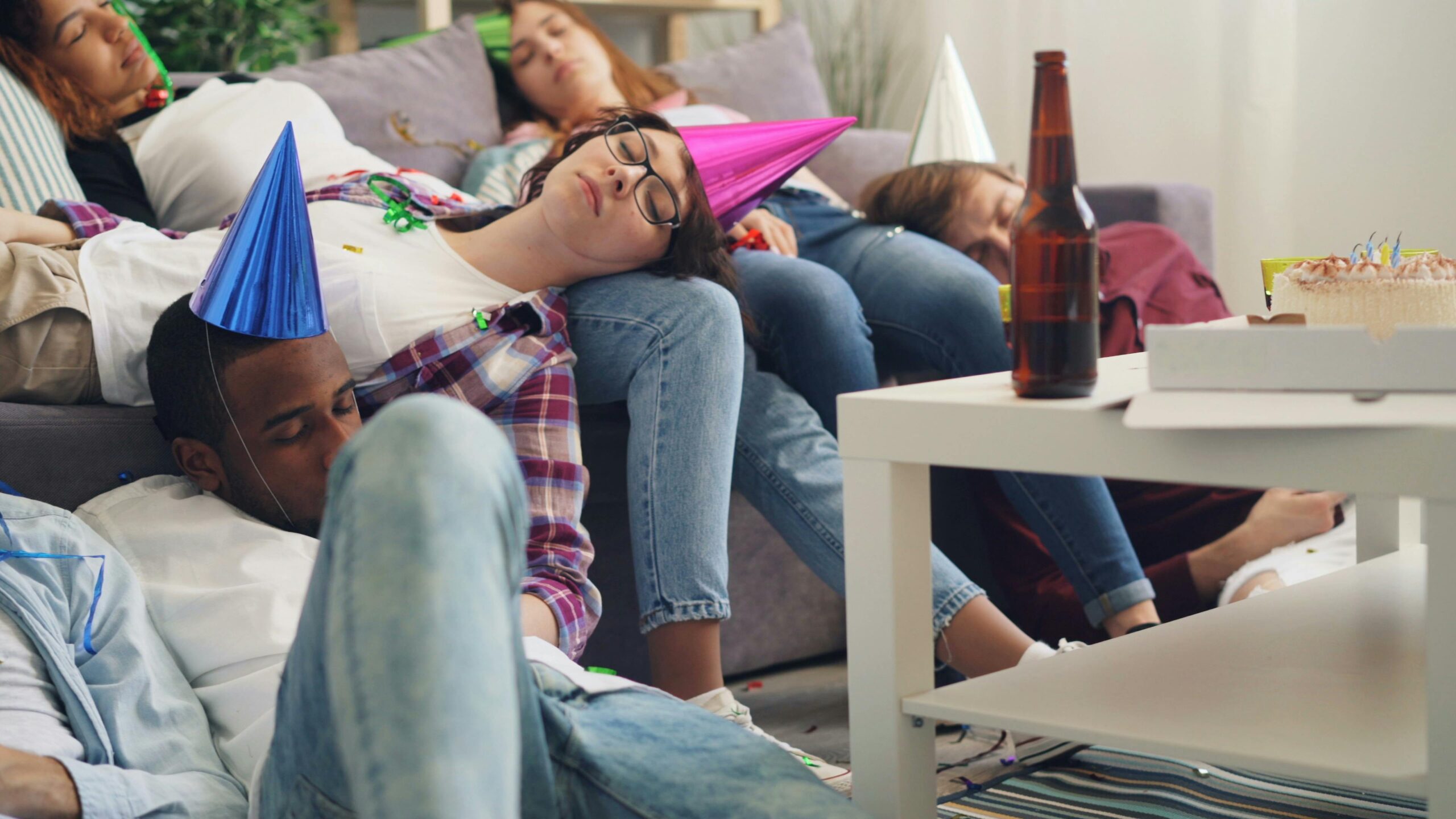 Young adults in party hats asleep in a living room after a celebration.