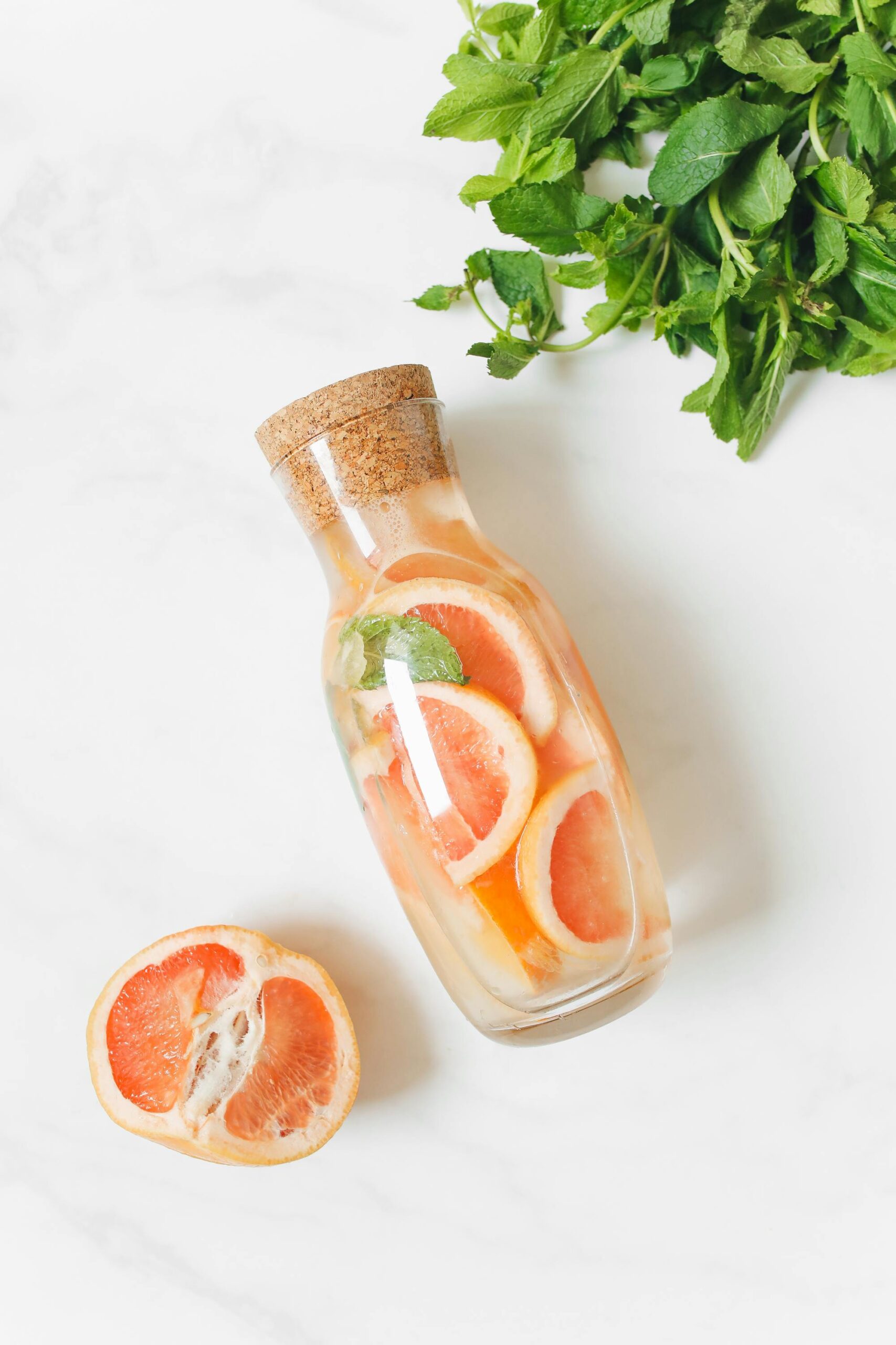 Top view of a corked bottle filled with citrus slices and mint leaves on a marble surface.