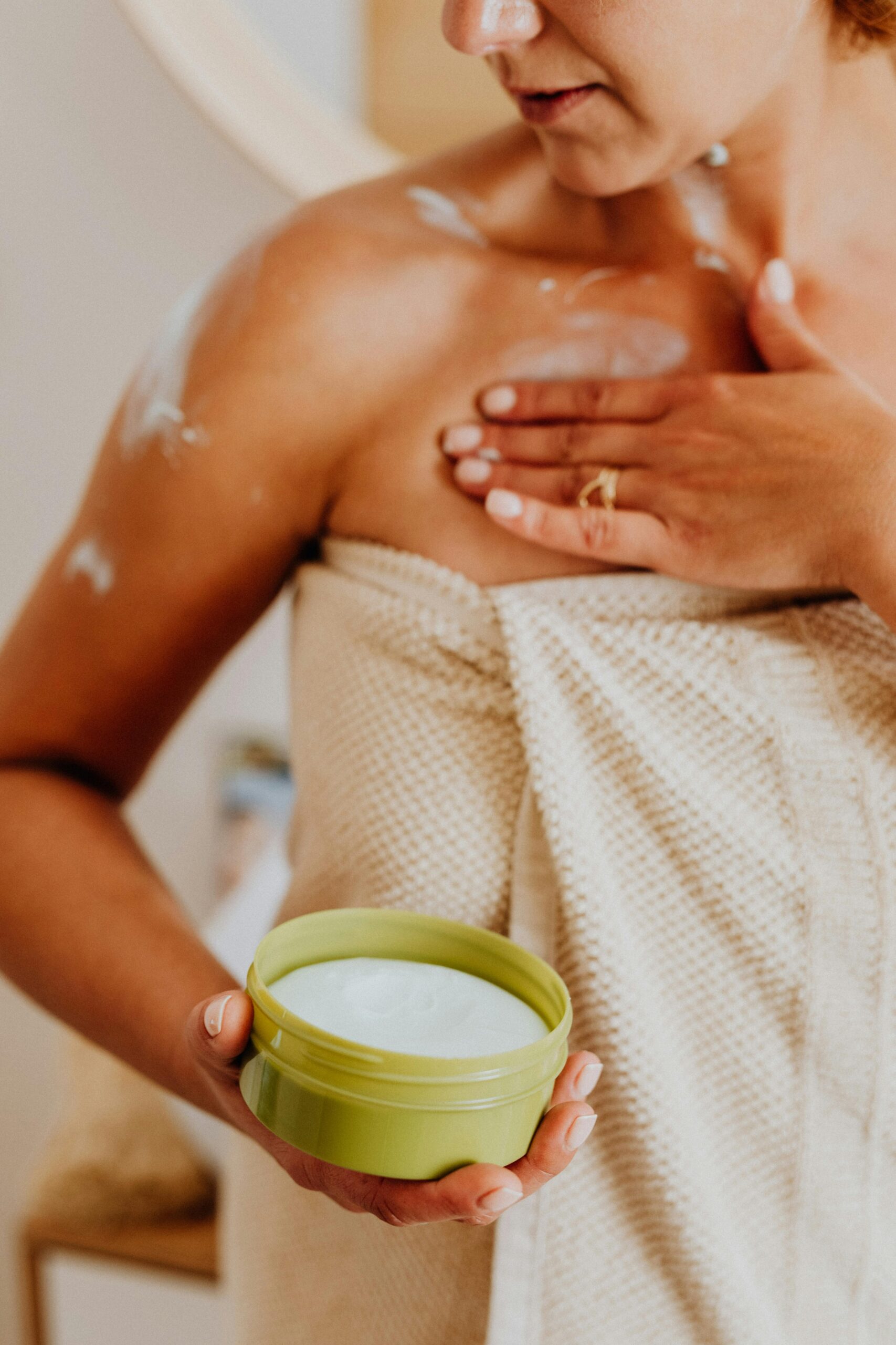 Close-up of woman applying body cream, enhancing skincare routine indoors.
