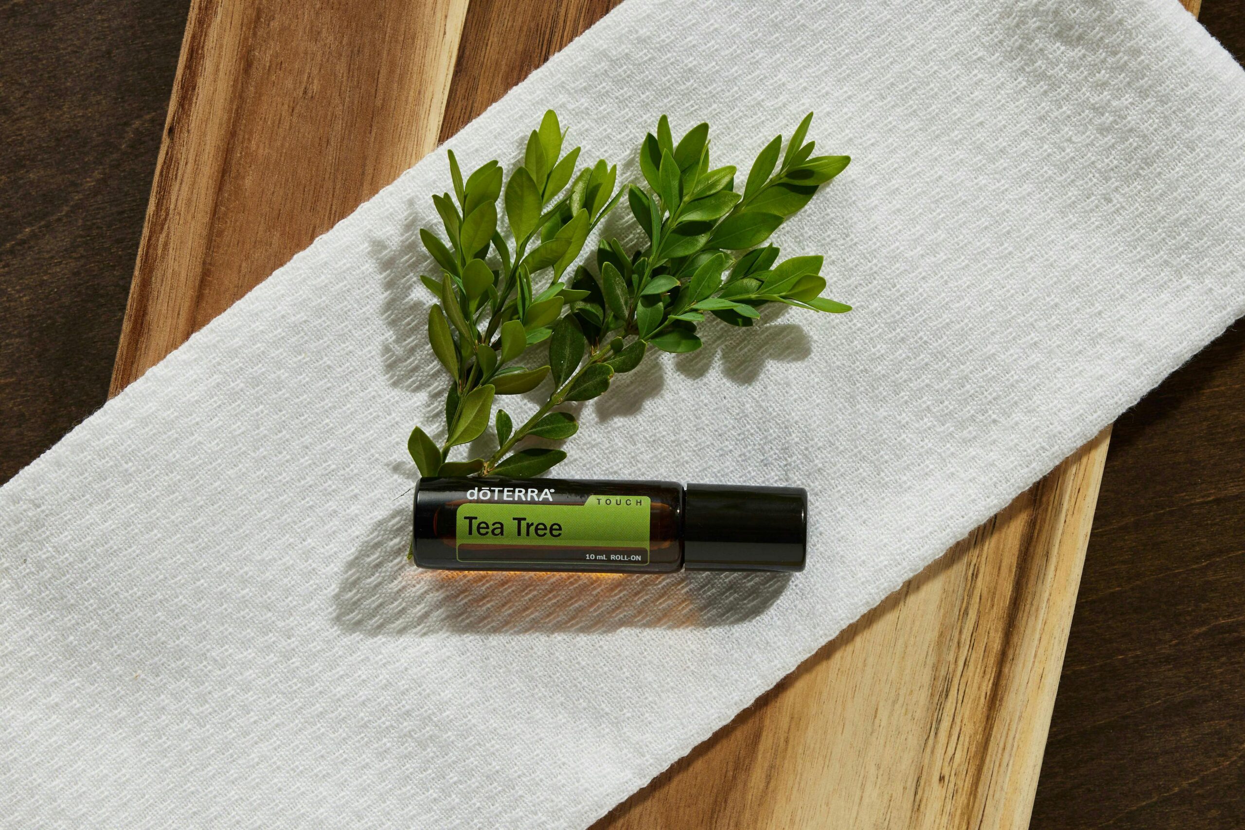 Tea tree oil bottle resting on white towel with green twig, highlighting natural beauty and wellness.