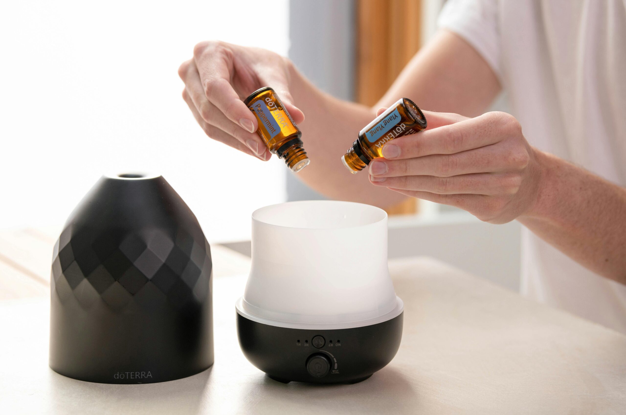 Hands preparing an essential oil diffuser with bottles for aromatherapy and wellness.