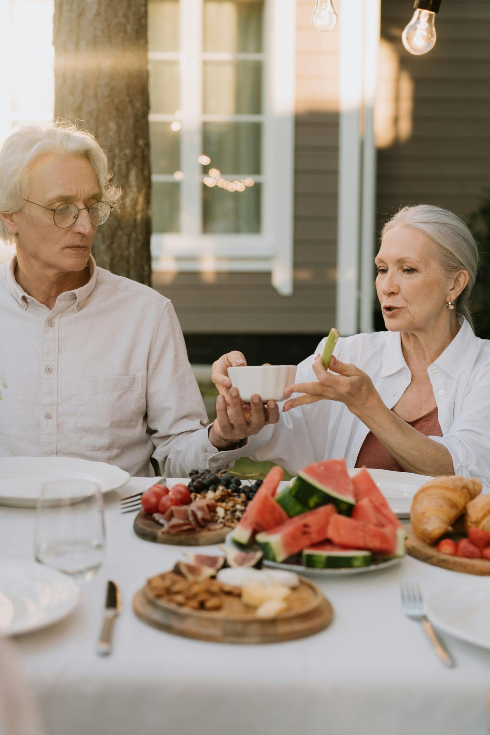 Elderly couple sharing a joyful meal outdoors in soft daylight.