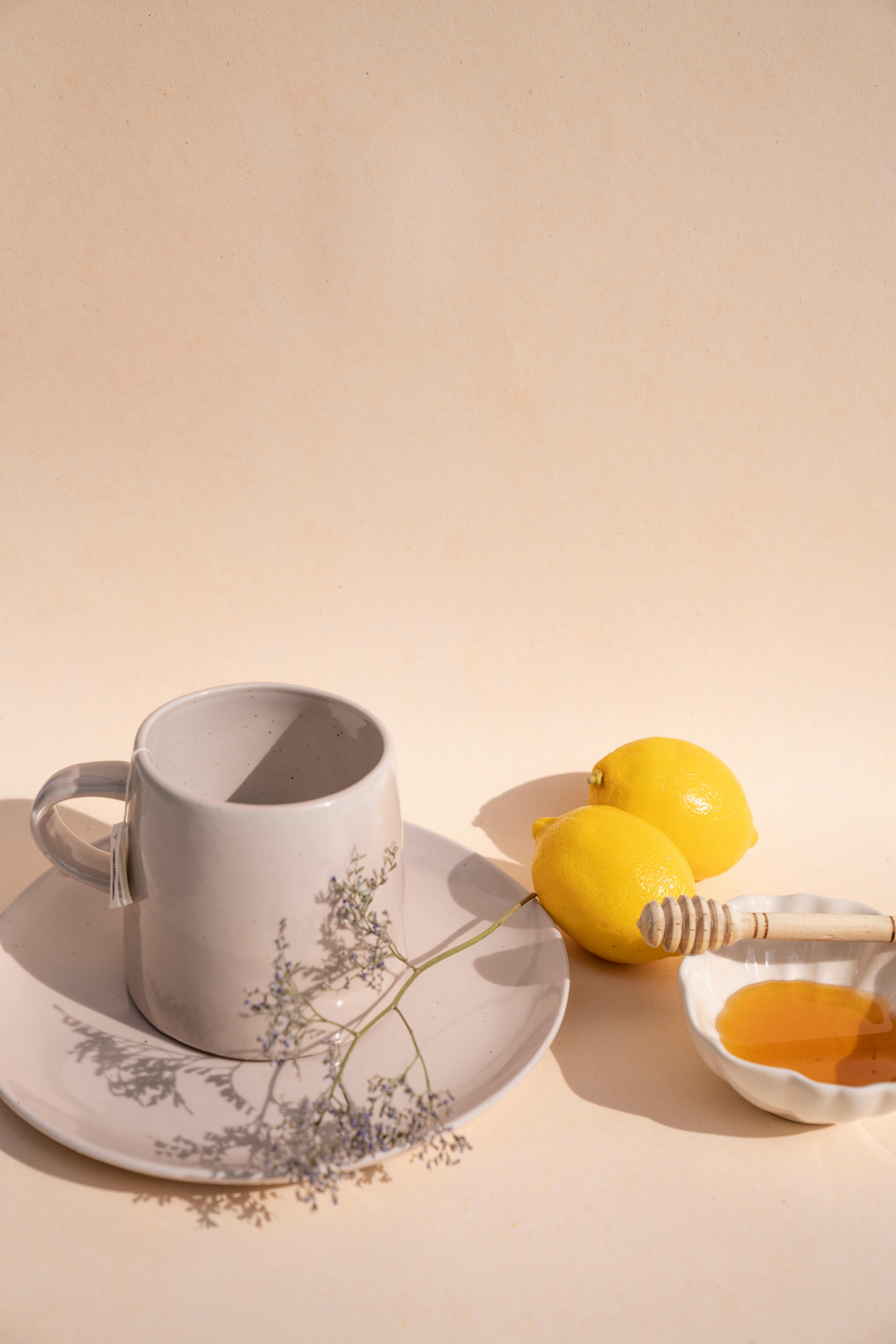 Minimalist setup featuring a ceramic cup, lemons, and honey on a flat surface.