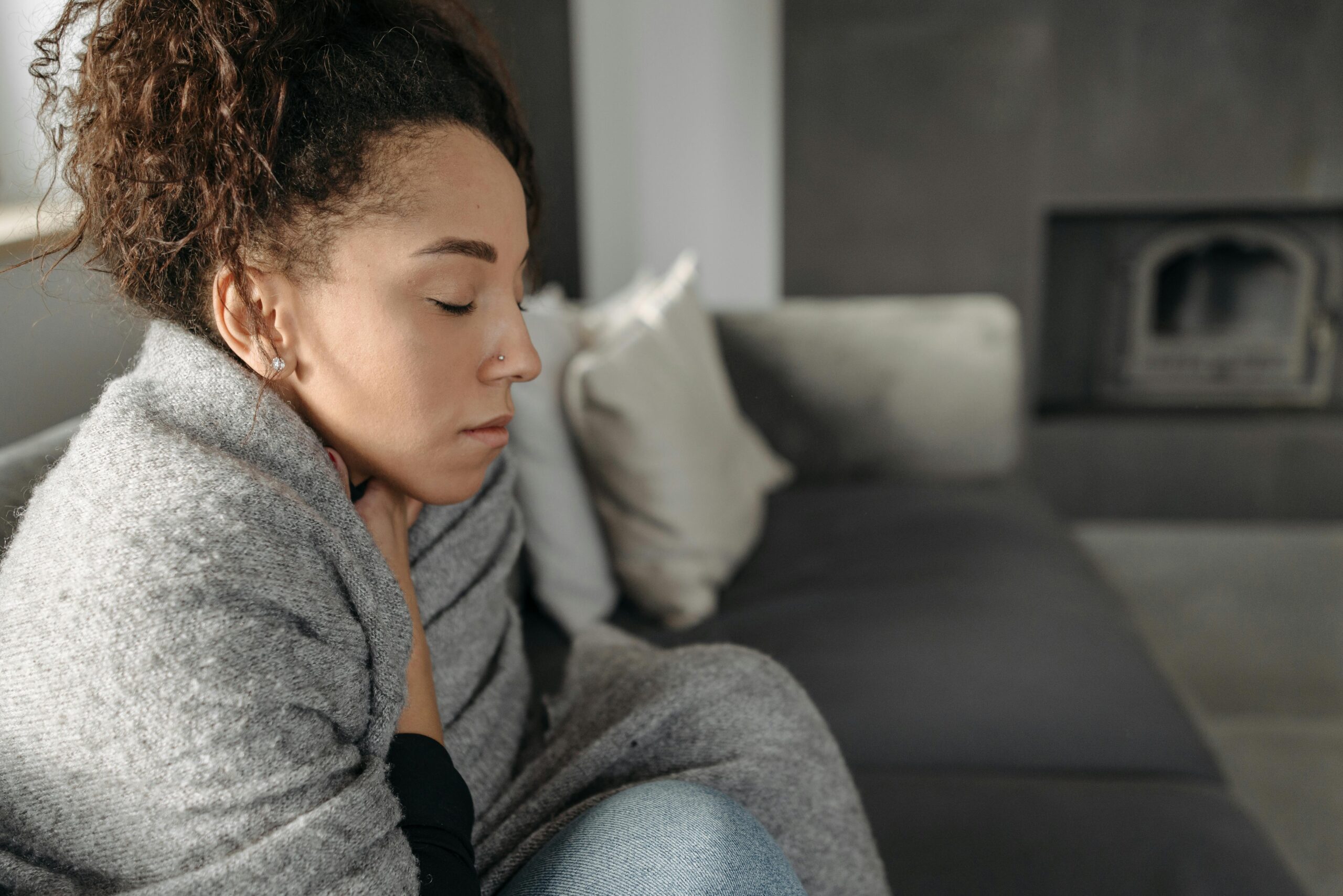Young woman resting at home, wrapped in a blanket and feeling unwell, conveying a sense of illness or discomfort.