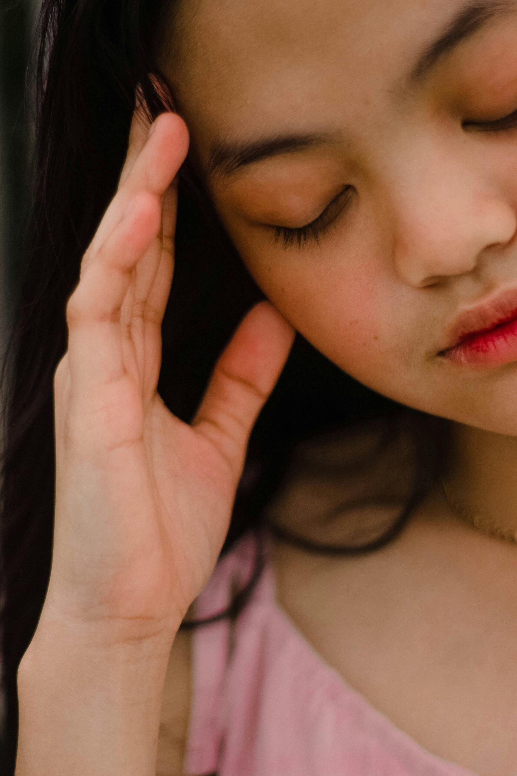 Close-up portrait of an Asian woman with closed eyes, expressing contemplation and tranquility.