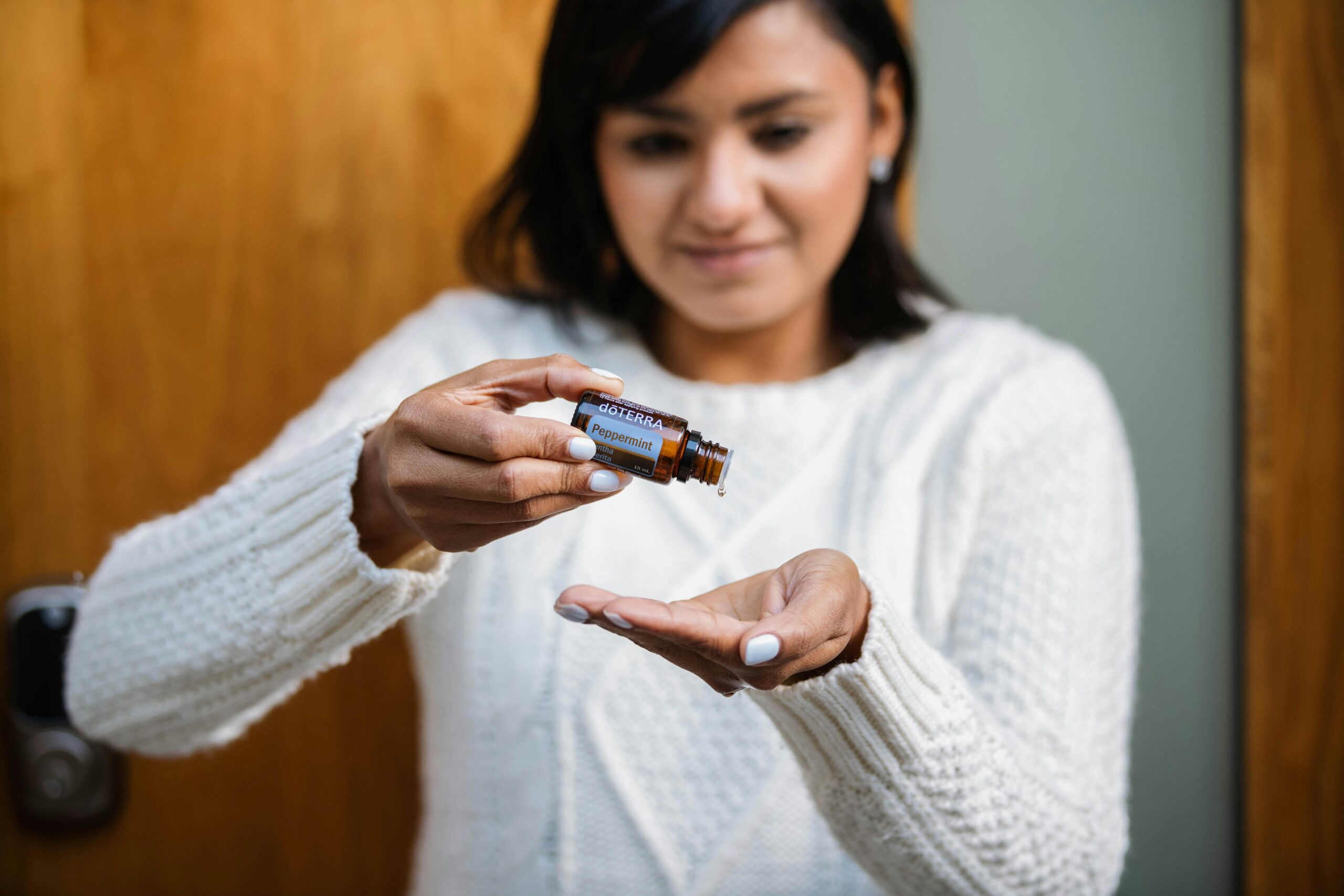 A woman pours peppermint essential oil into her hand indoors, focusing on aromatherapy.