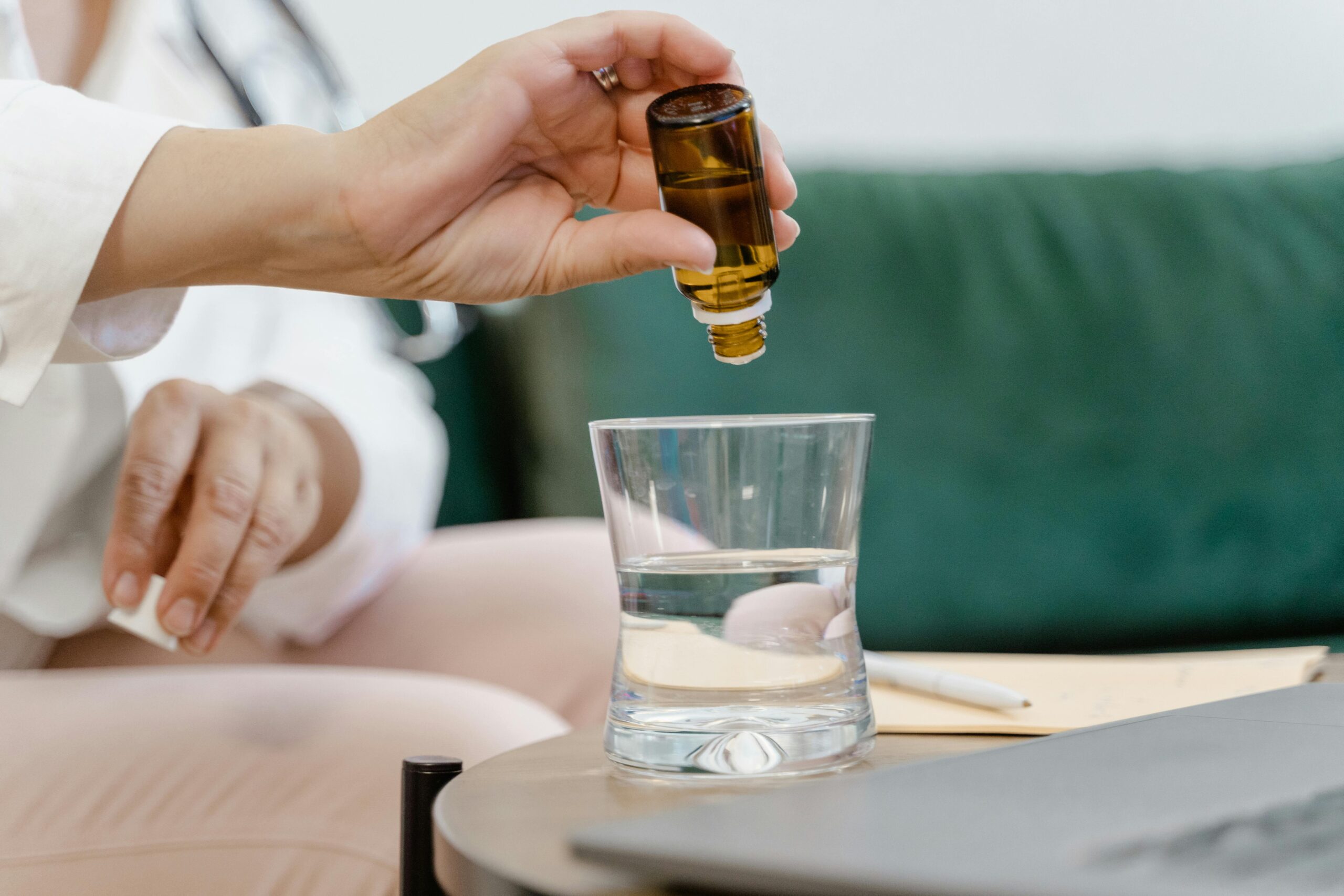 Hand pouring essential oil into a glass of water, symbolizing relaxation and therapy.