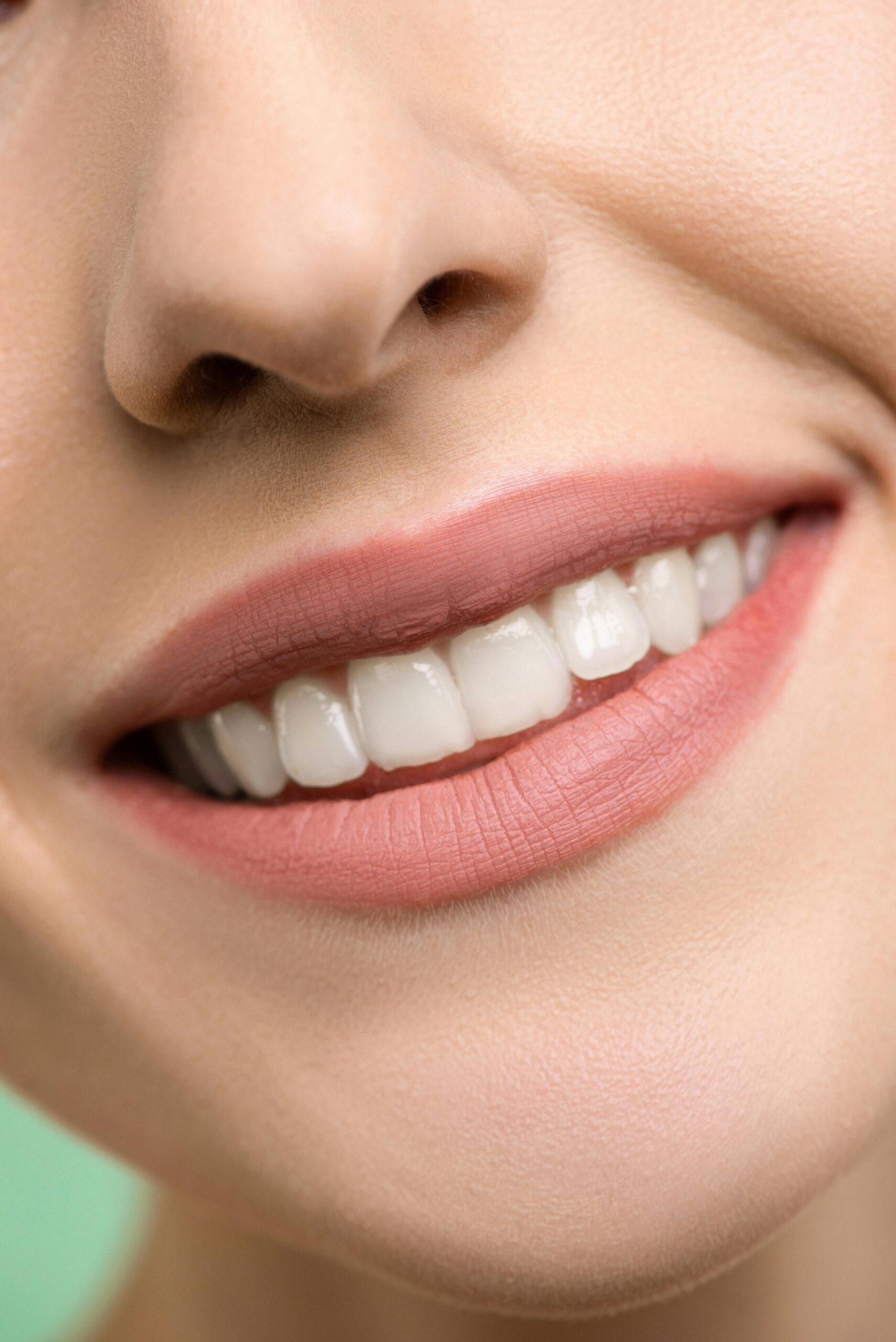 A close-up image focusing on a woman's smiling mouth, showing white teeth and pink lips.