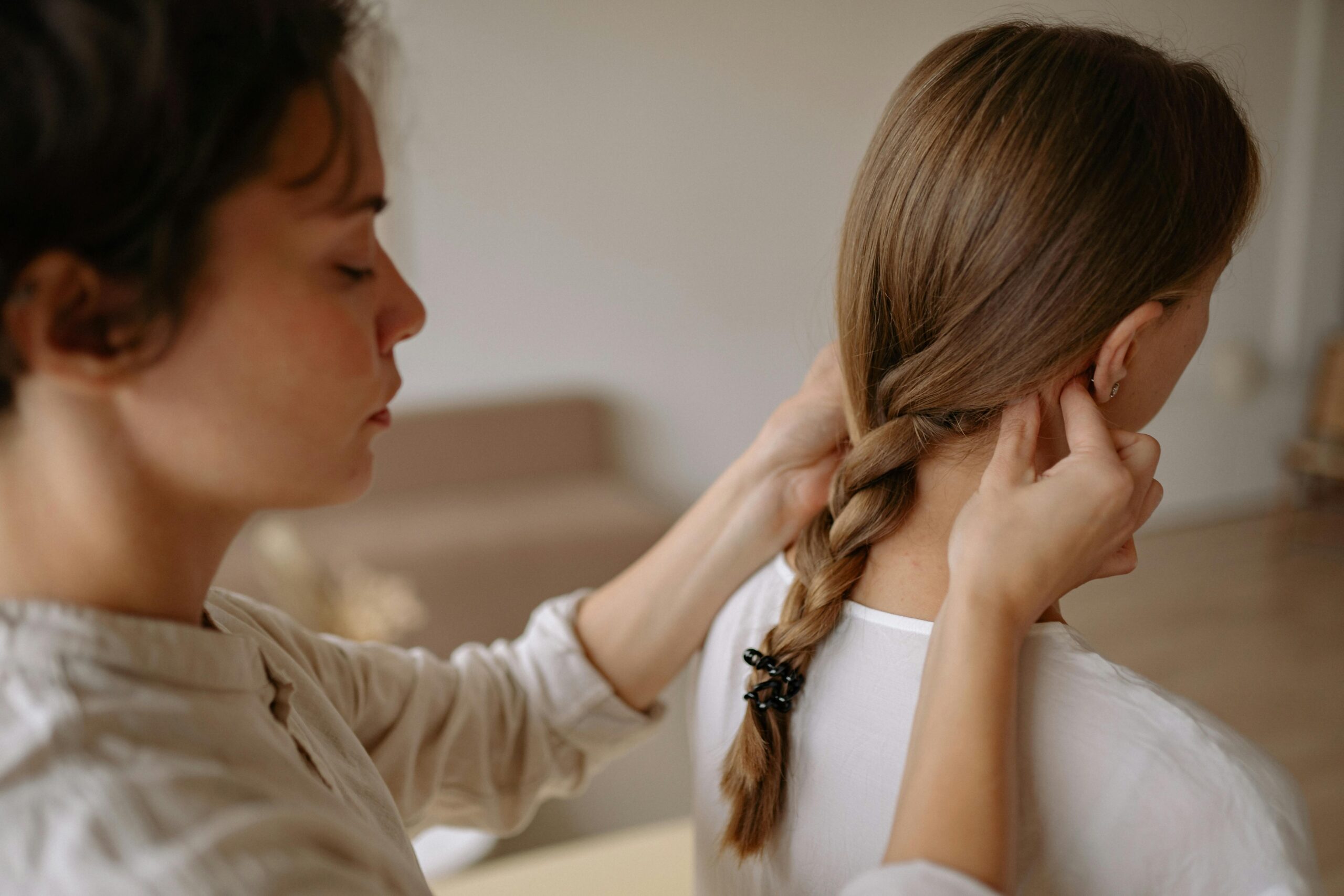 Close-up of a woman braiding another woman's hair indoors, evoking tranquility.