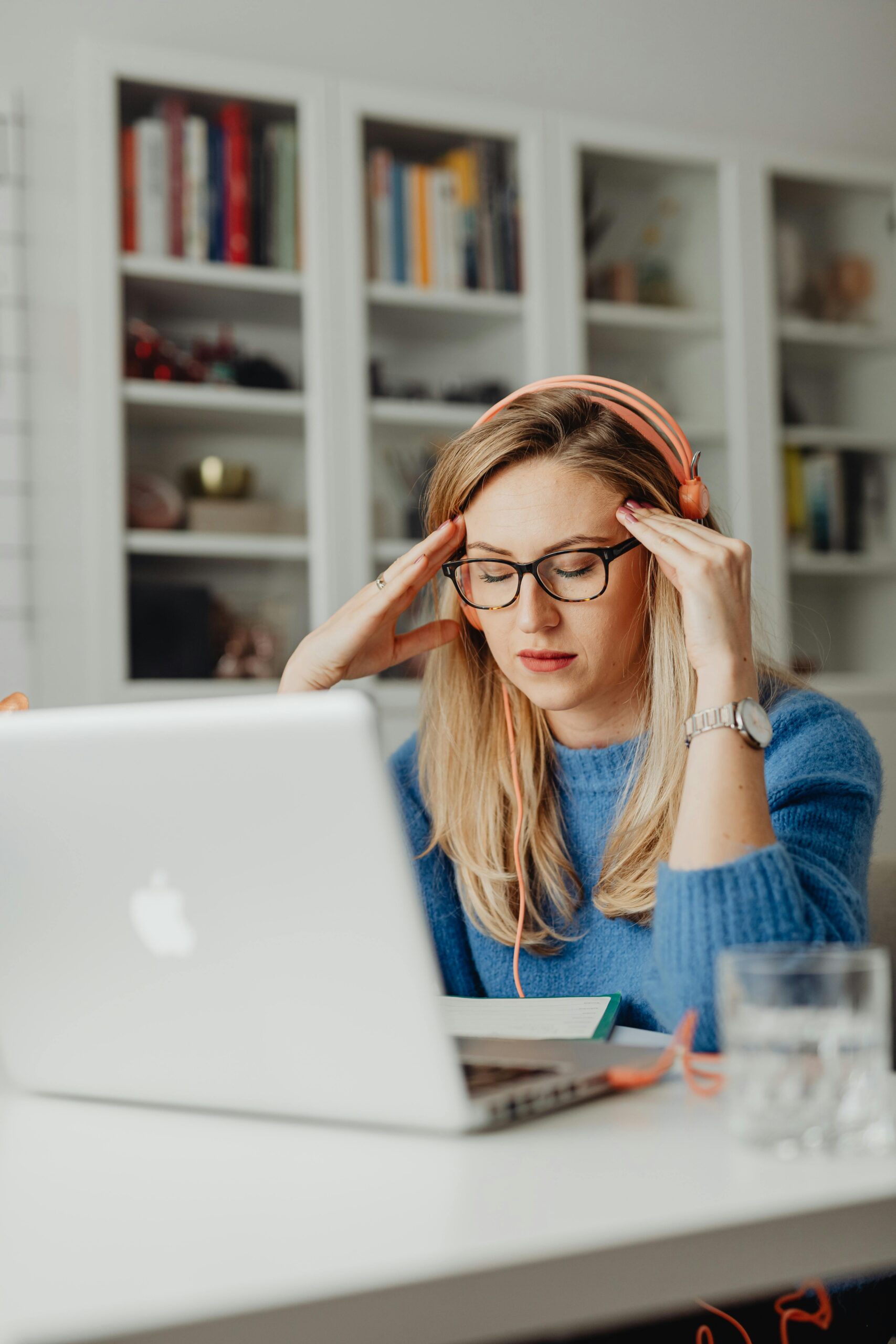 Woman with blond hair and glasses experiencing stress while working from home on a laptop.