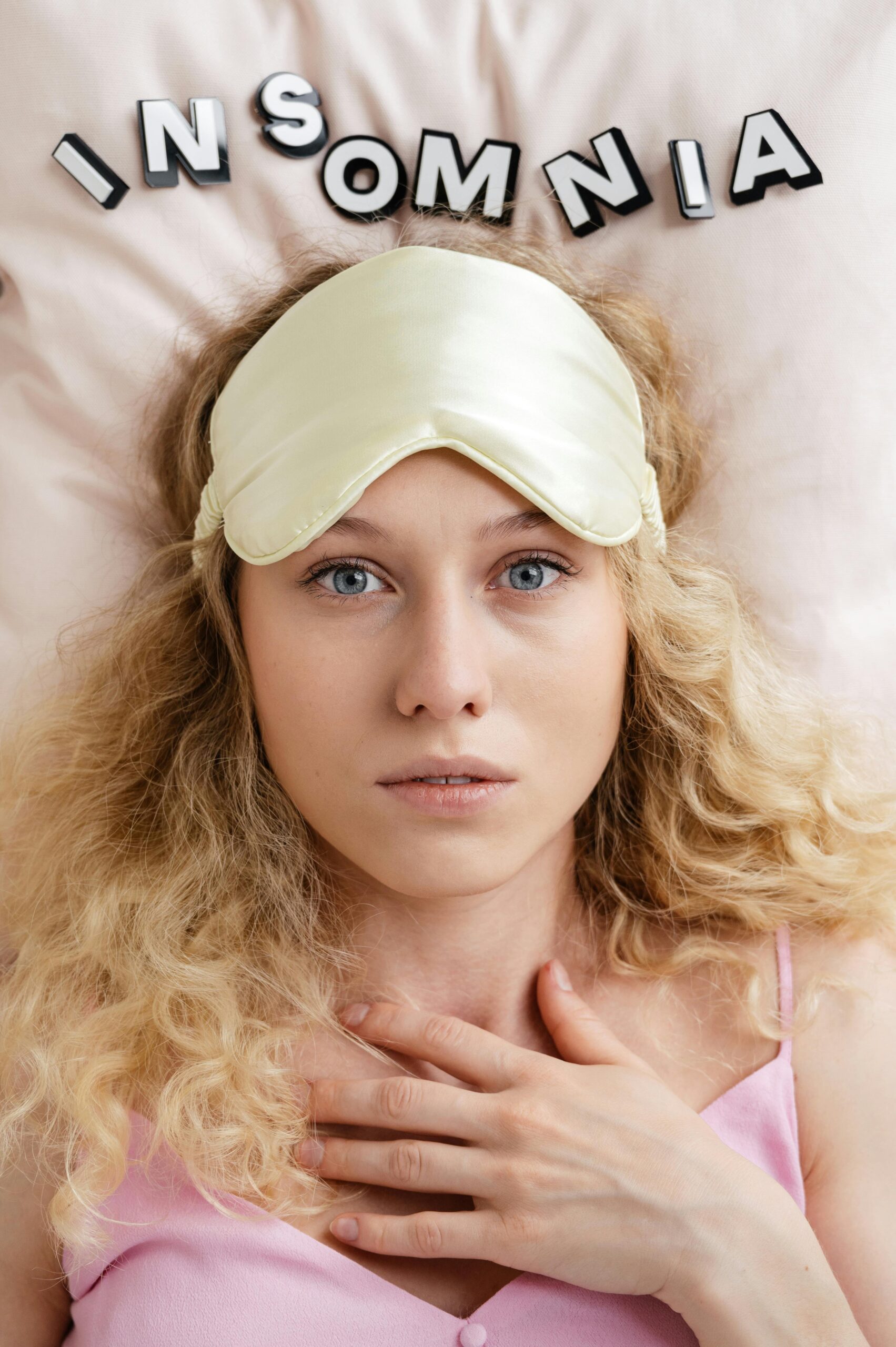 Blonde woman wearing a sleep mask, looking awake and worried, highlighting insomnia.