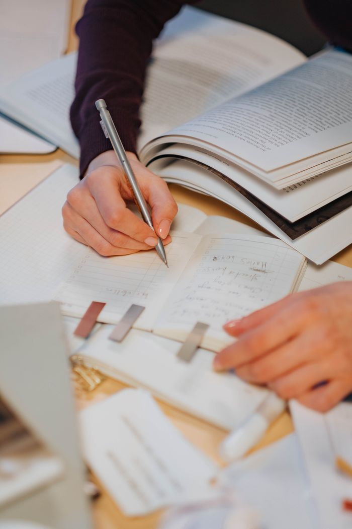 Close-up of hands writing notes in a study environment with open books.