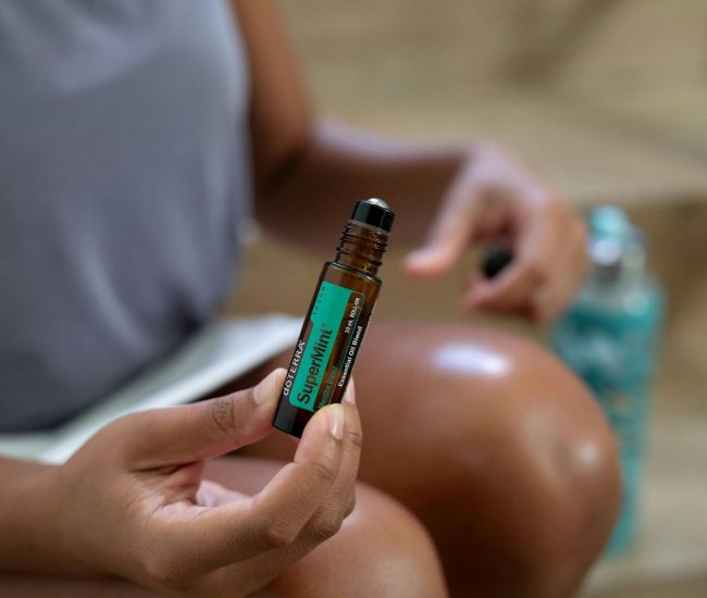 A woman holding a roller bottle of doTERRA SuperMint essential oil close-up shot.