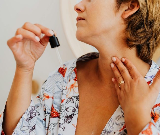 Woman in a floral robe applying skincare serum with a dropper indoors.